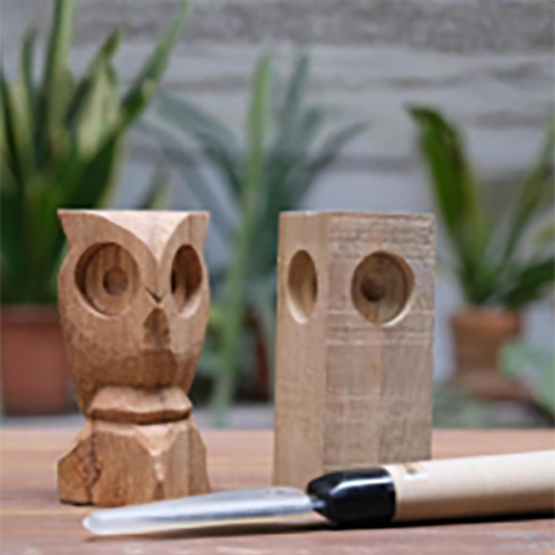 A carved wooden owl figure beside a rough block and a carving knife