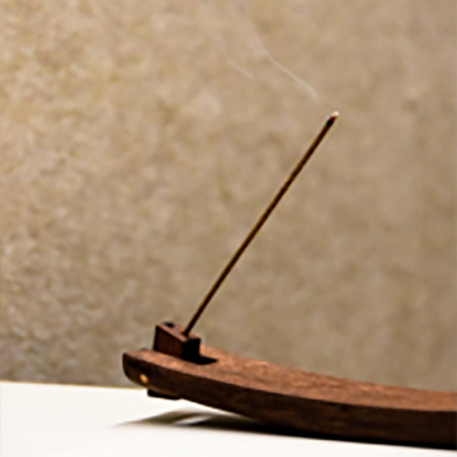 A curved dark wood incense holder with a lit incense stick