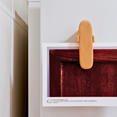 A small wooden note keeper clipped to the corner of a framed picture