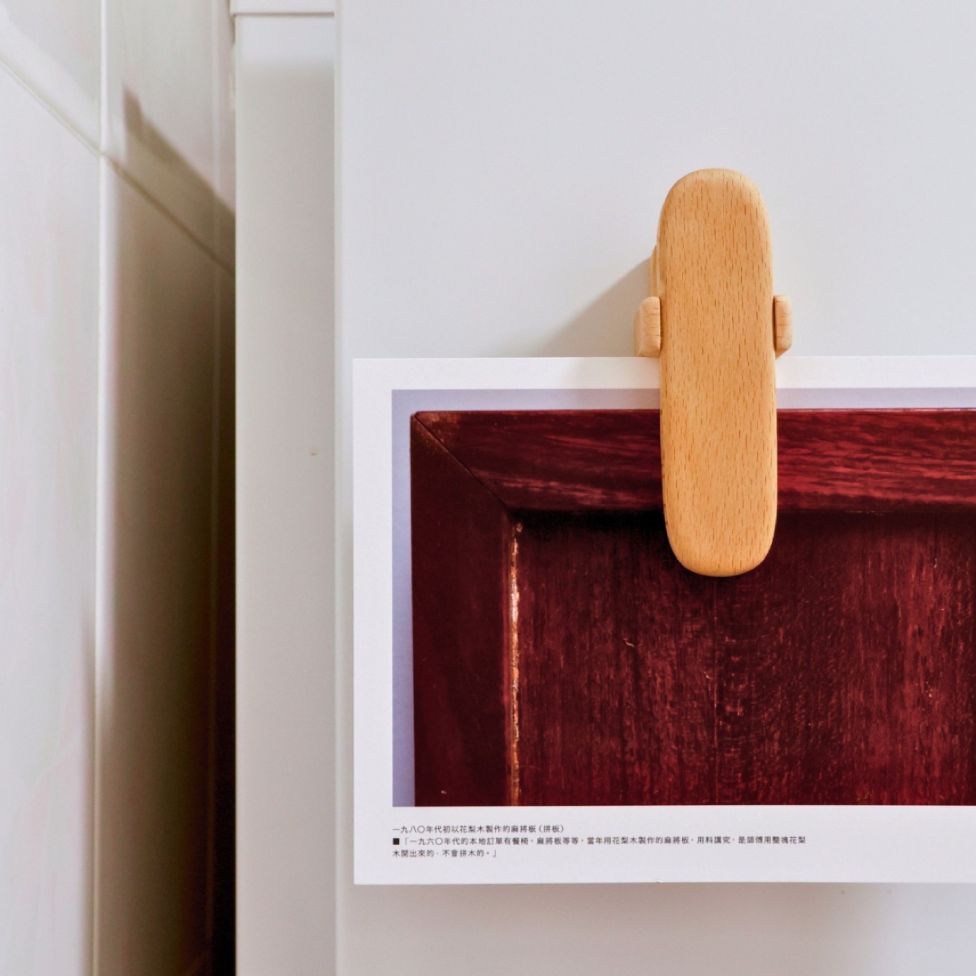 A pale wooden clip gripping the top edge of a photo print against a white wall