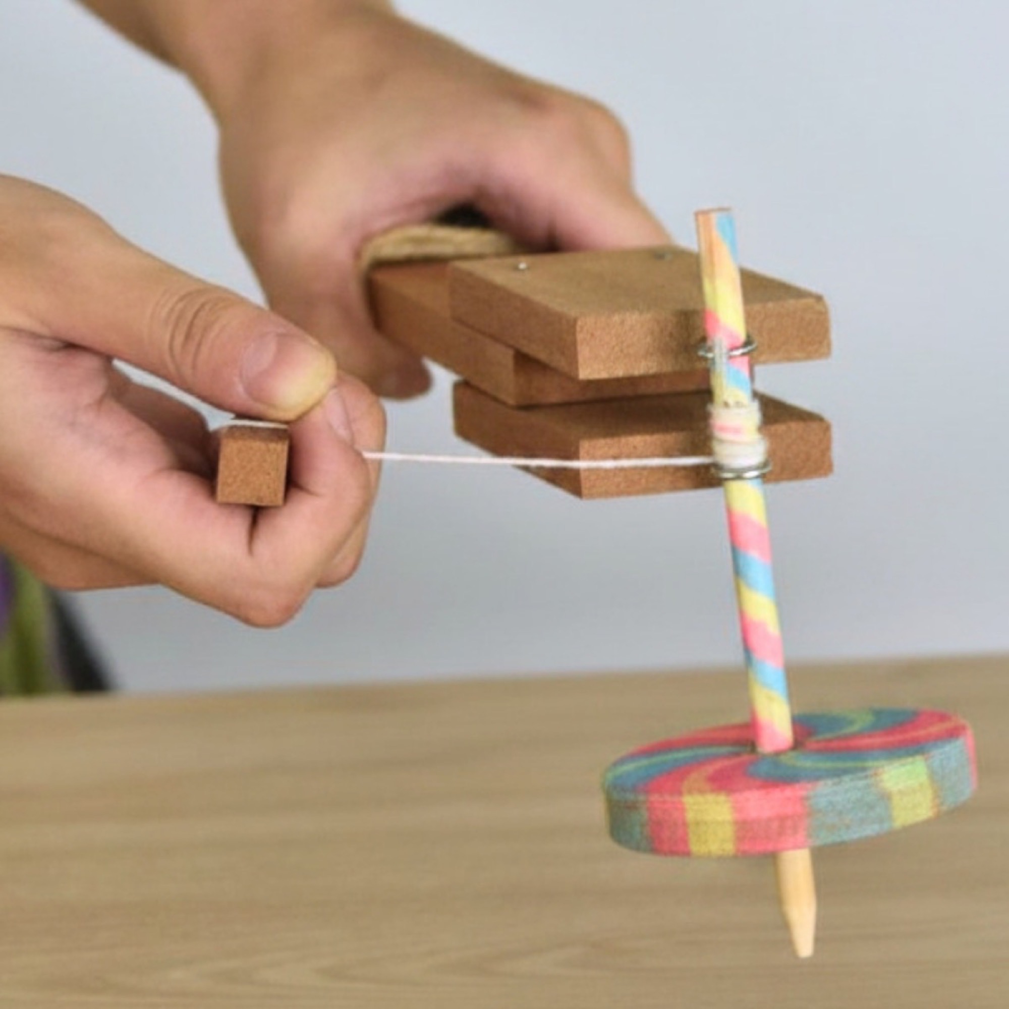 Two finished wooden spinning tops – one rainbow-striped, one red with a green star – beside the wooden launcher on a table